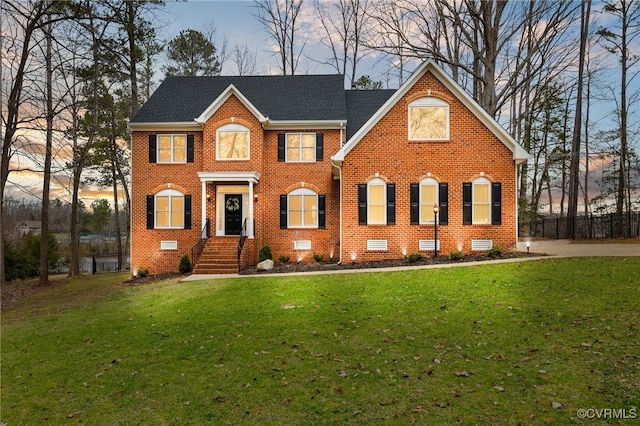 colonial home featuring crawl space, brick siding, a lawn, and a shingled roof