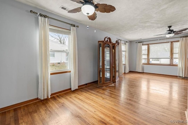 empty room with baseboards, visible vents, ceiling fan, a textured ceiling, and light wood-type flooring