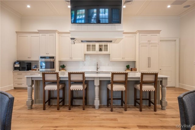 kitchen featuring a center island with sink, backsplash, a high ceiling, and stainless steel oven