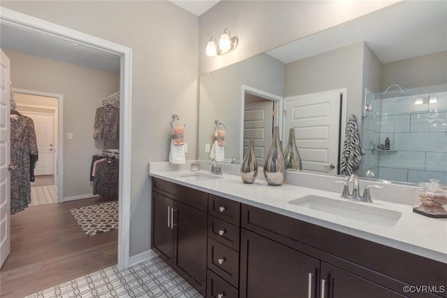 full bathroom featuring a sink, double vanity, a spacious closet, and a tile shower