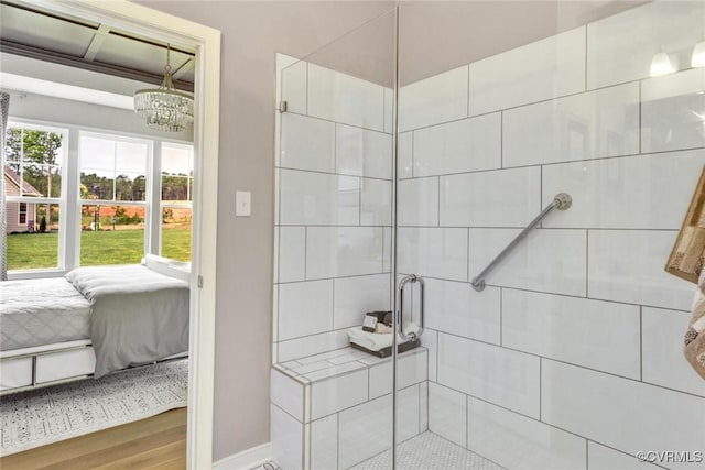 ensuite bathroom featuring wood finished floors, a notable chandelier, tiled shower, and connected bathroom