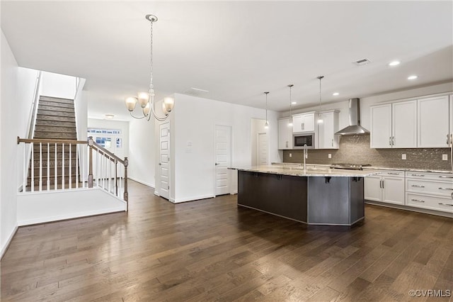 kitchen featuring built in microwave, wall chimney exhaust hood, decorative backsplash, and white cabinets