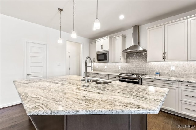 kitchen featuring stainless steel range with gas cooktop, built in microwave, an island with sink, wall chimney exhaust hood, and a sink