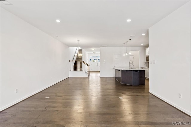 unfurnished living room featuring a sink, dark wood finished floors, recessed lighting, baseboards, and stairs