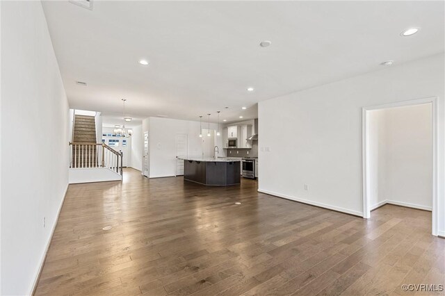 unfurnished living room with dark wood-style floors, a notable chandelier, recessed lighting, and a sink