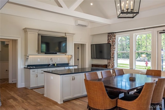 kitchen featuring dark countertops, a center island, an AC wall unit, wood finished floors, and a sink