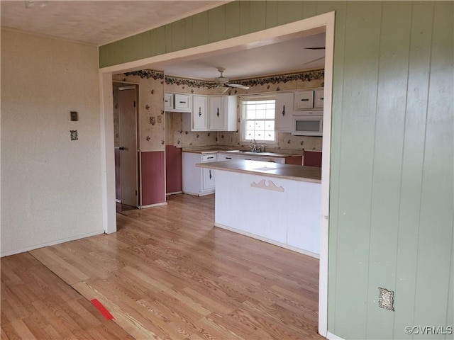 kitchen with ceiling fan, light wood-style flooring, a peninsula, and white cabinets