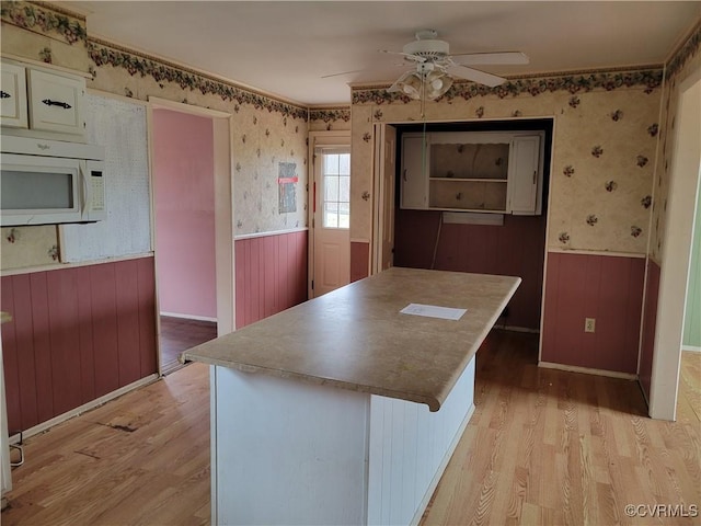 kitchen with white microwave, wainscoting, wallpapered walls, and light wood-style floors