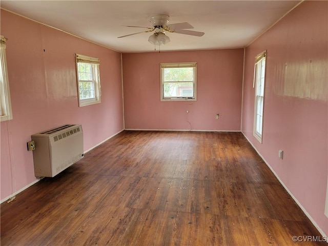 empty room featuring dark wood finished floors, heating unit, a wealth of natural light, and ceiling fan