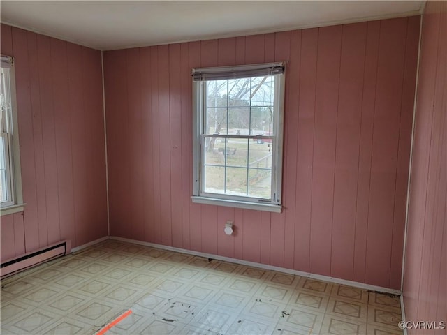 unfurnished room with a baseboard heating unit, light floors, baseboards, and a wealth of natural light