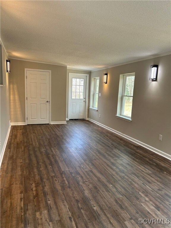 empty room with crown molding, baseboards, dark wood-style flooring, and a textured ceiling