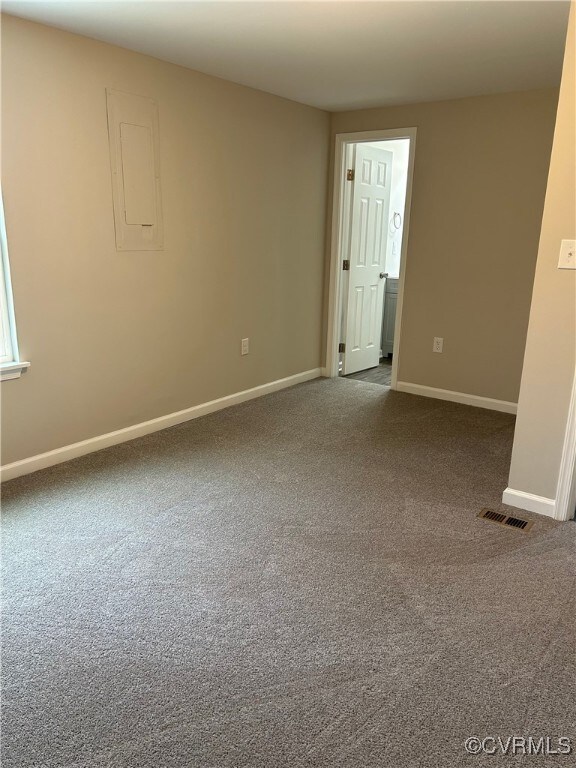 carpeted spare room featuring electric panel, visible vents, and baseboards