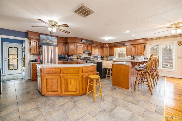 kitchen with visible vents, freestanding refrigerator, ceiling fan, under cabinet range hood, and range