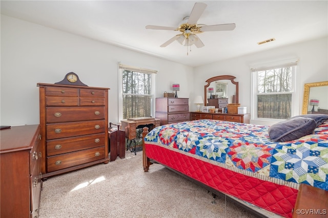 bedroom with ceiling fan, multiple windows, visible vents, and light carpet