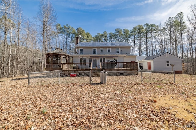 view of front of home featuring fence, a wooden deck, a chimney, a gazebo, and metal roof