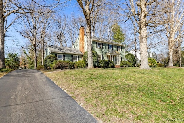 colonial inspired home with a front lawn, aphalt driveway, and a chimney