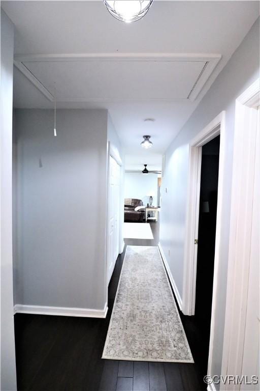 hallway featuring dark wood finished floors, attic access, and baseboards