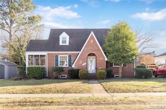 view of front of property featuring a storage shed, a front lawn, an outbuilding, and brick siding