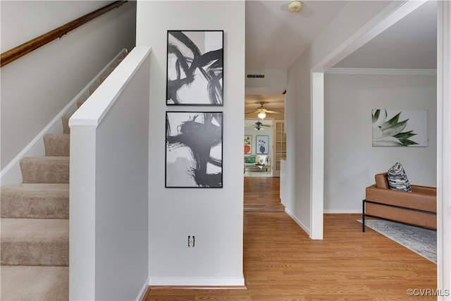 hallway featuring visible vents, baseboards, stairs, ornamental molding, and light wood-style floors