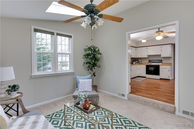 living area featuring a skylight, visible vents, light colored carpet, and ceiling fan