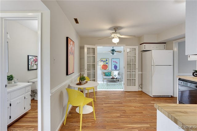 kitchen with light wood-type flooring, a ceiling fan, black dishwasher, freestanding refrigerator, and french doors