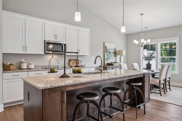 kitchen with stainless steel microwave, vaulted ceiling, wood finished floors, and a sink