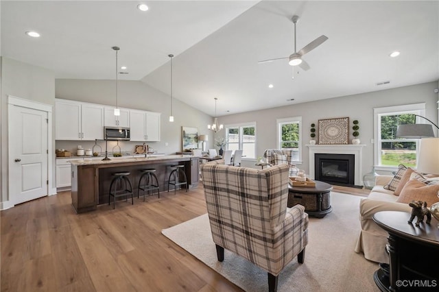 living room with a glass covered fireplace, a wealth of natural light, light wood-style flooring, and ceiling fan with notable chandelier