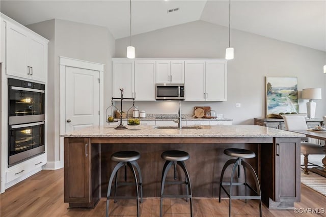 kitchen featuring wood finished floors, lofted ceiling, a sink, stainless steel appliances, and white cabinetry