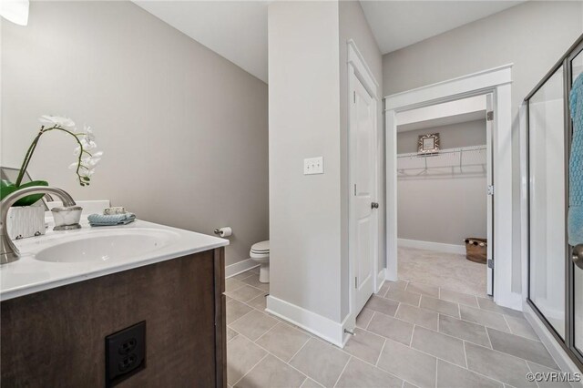 bathroom featuring a walk in closet, tile patterned floors, baseboards, and a stall shower