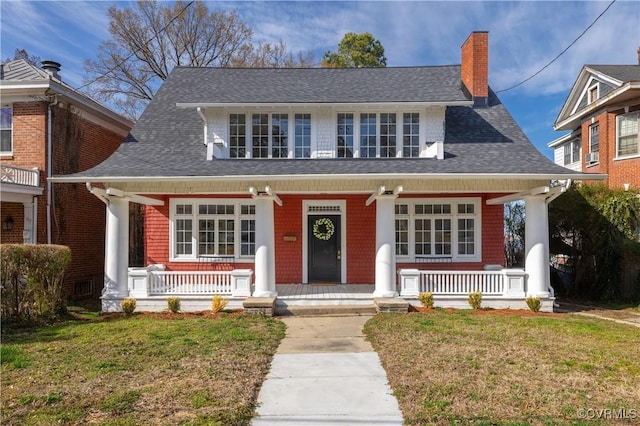 view of front facade with a porch, a chimney, a front yard, and a shingled roof