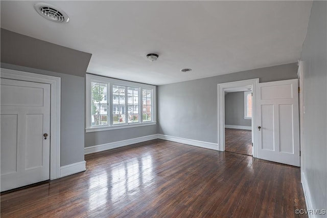 unfurnished room with visible vents, plenty of natural light, dark wood-type flooring, and baseboards