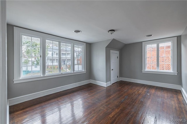 spare room featuring lofted ceiling, baseboards, visible vents, and dark wood-style flooring