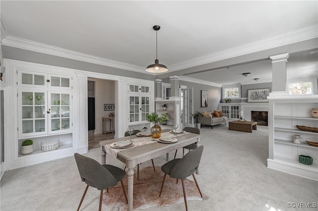 dining space featuring light carpet, crown molding, a fireplace, and ornate columns