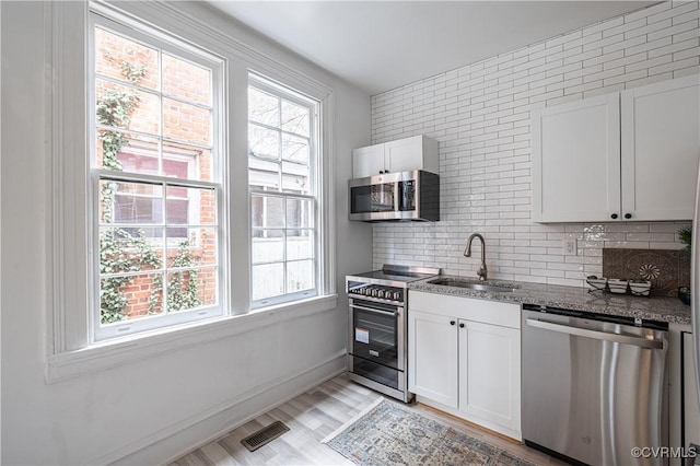 kitchen featuring visible vents, stone counters, a sink, stainless steel appliances, and tasteful backsplash