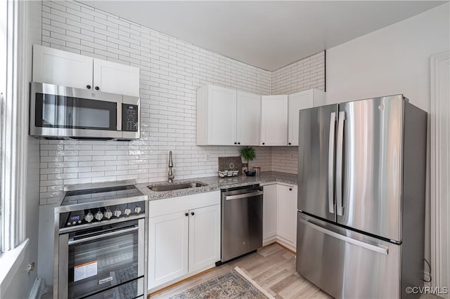 kitchen with light stone countertops, appliances with stainless steel finishes, light wood-style floors, white cabinets, and a sink