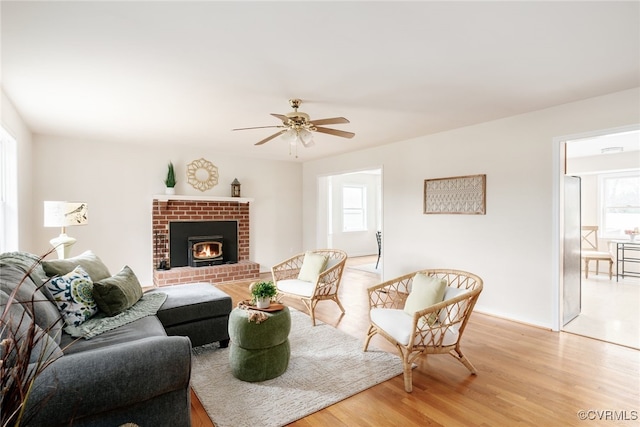 living area with a ceiling fan, a brick fireplace, and light wood-style floors