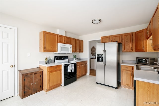 kitchen featuring white microwave, electric range, a sink, light countertops, and stainless steel fridge