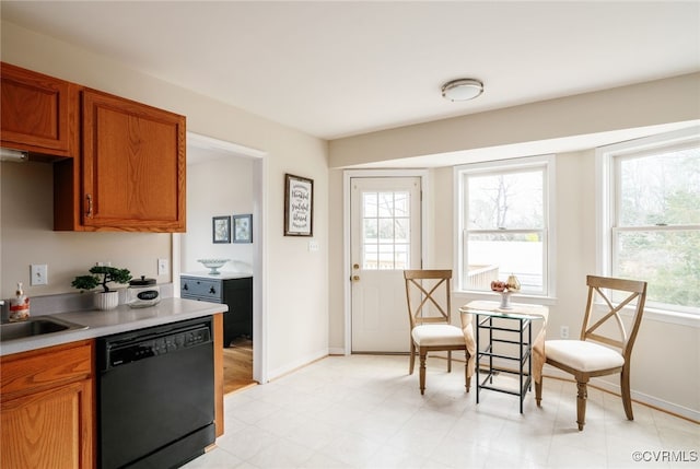 kitchen with brown cabinets, a sink, black dishwasher, light countertops, and baseboards