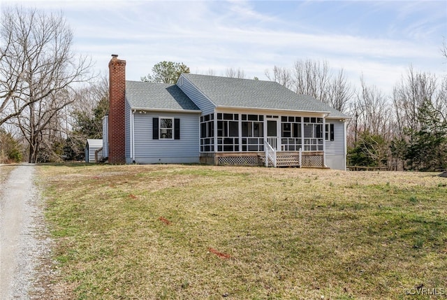 back of property with driveway, a yard, a sunroom, a shingled roof, and a chimney