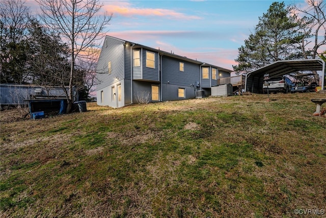 back of house at dusk with a carport and a yard