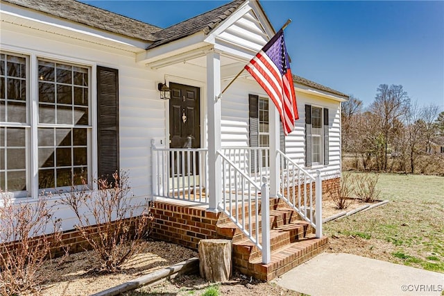 view of exterior entry featuring covered porch and a shingled roof