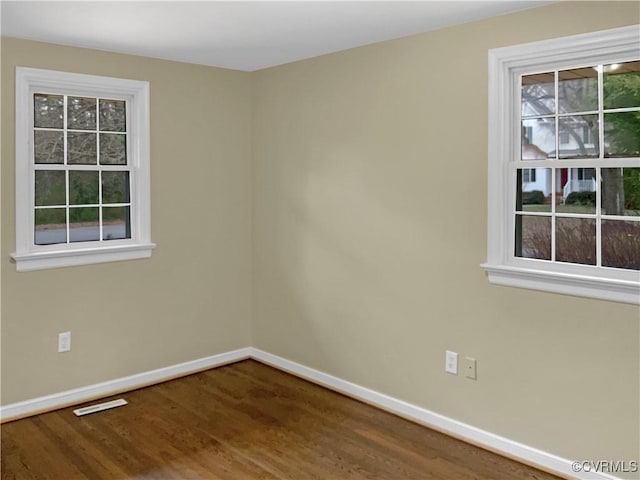 empty room with a wealth of natural light, baseboards, and wood finished floors