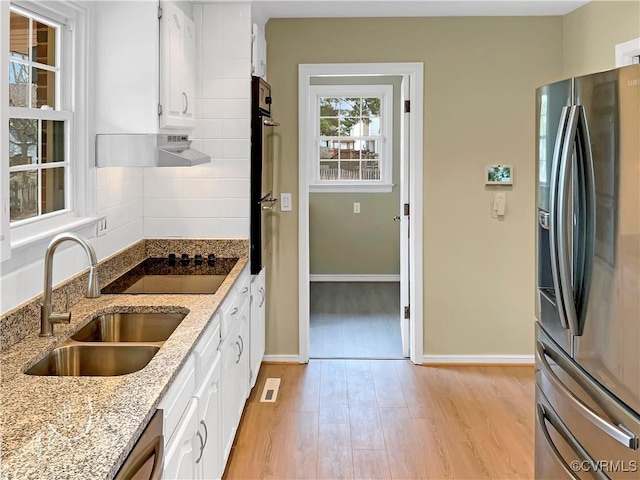 kitchen featuring stainless steel refrigerator with ice dispenser, a sink, under cabinet range hood, white cabinetry, and light wood-style floors