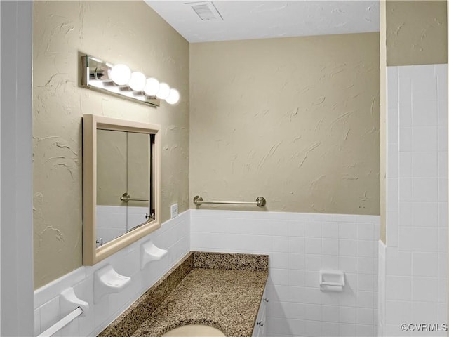 bathroom featuring visible vents, vanity, tile walls, and a textured wall