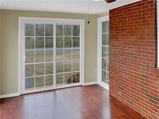 spare room with baseboards, a healthy amount of sunlight, brick wall, and dark wood-style flooring