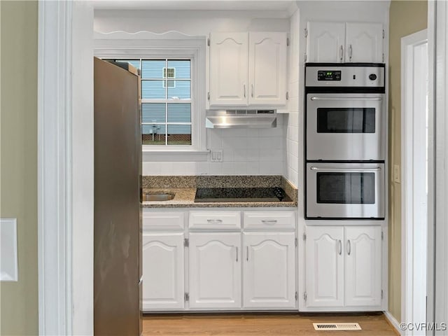 kitchen featuring visible vents, stainless steel double oven, white cabinets, under cabinet range hood, and black electric cooktop