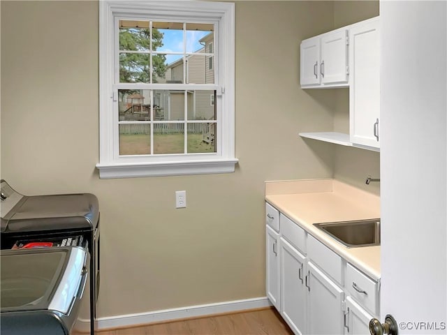 washroom featuring baseboards, cabinet space, a sink, light wood-style floors, and independent washer and dryer