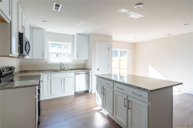 kitchen with a sink, a kitchen island, wood finished floors, appliances with stainless steel finishes, and light stone countertops