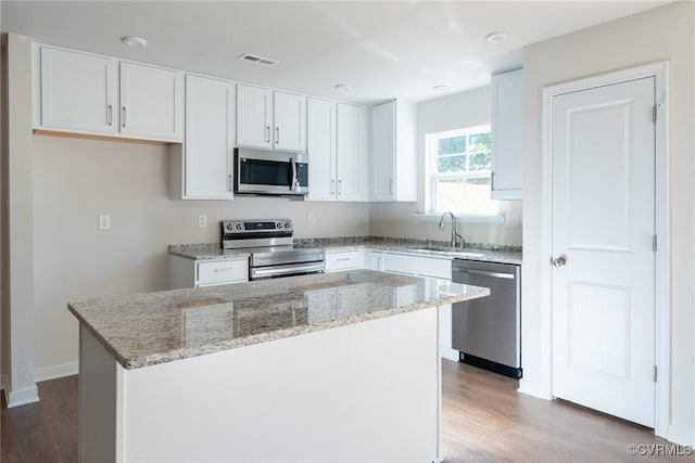 kitchen featuring a sink, light stone counters, a kitchen island, white cabinetry, and stainless steel appliances