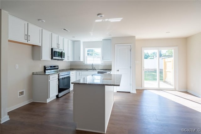 kitchen with visible vents, stone countertops, a sink, appliances with stainless steel finishes, and a center island